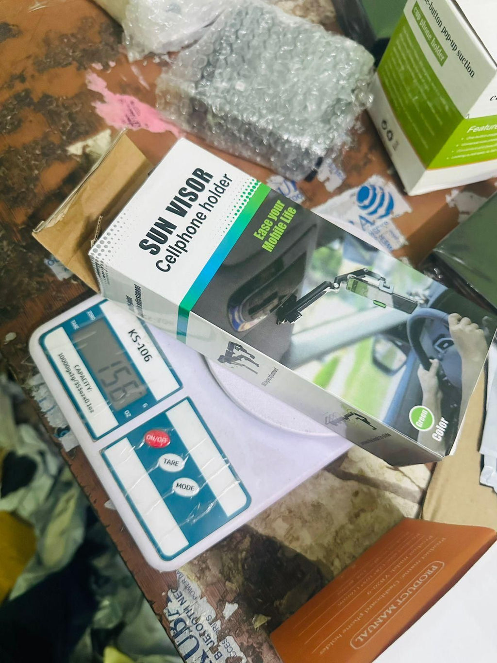 Sun visor phone holder packaging on a cluttered surface with a digital scale.